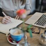 person-writing-on-a-notebook-beside-macbook-1766604
